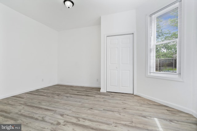 unfurnished bedroom featuring light wood-type flooring, a closet, and multiple windows