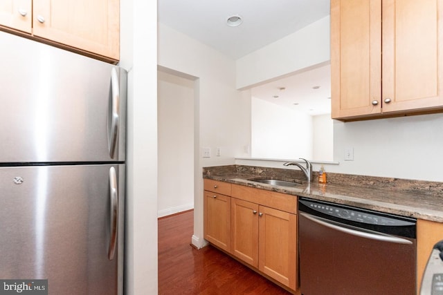 kitchen featuring appliances with stainless steel finishes, sink, dark stone counters, dark hardwood / wood-style floors, and light brown cabinets