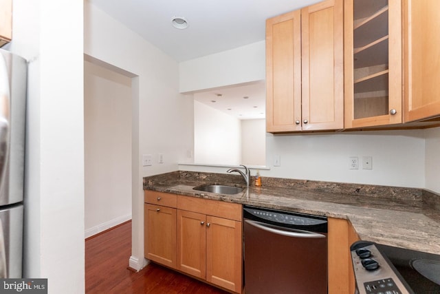 kitchen with dishwasher, sink, dark wood-type flooring, dark stone counters, and stainless steel fridge