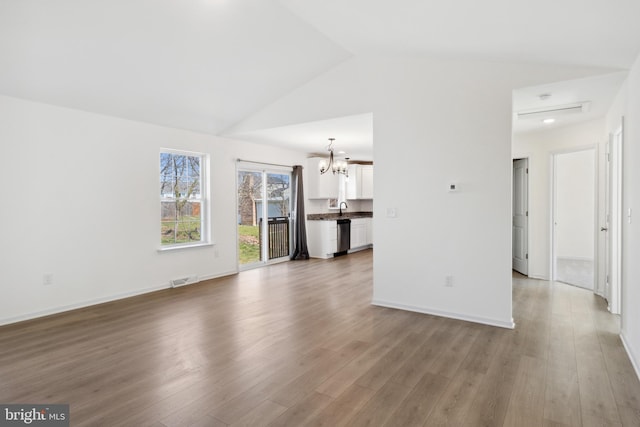 unfurnished living room with light hardwood / wood-style floors, vaulted ceiling, a chandelier, and sink