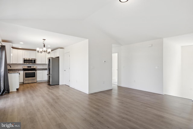 unfurnished living room featuring an inviting chandelier, vaulted ceiling, and light hardwood / wood-style flooring