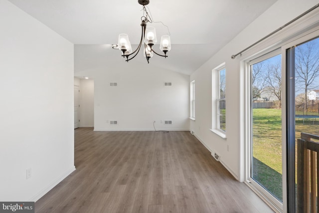 unfurnished dining area with vaulted ceiling, a wealth of natural light, a chandelier, and wood-type flooring