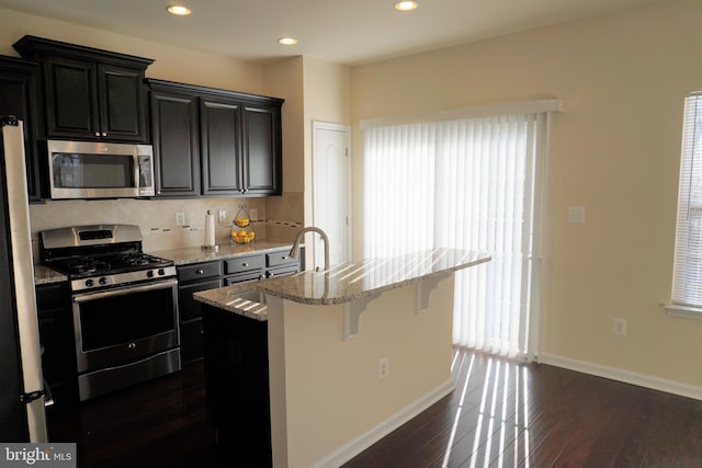 kitchen with a center island with sink, stainless steel appliances, a wealth of natural light, a breakfast bar, and sink