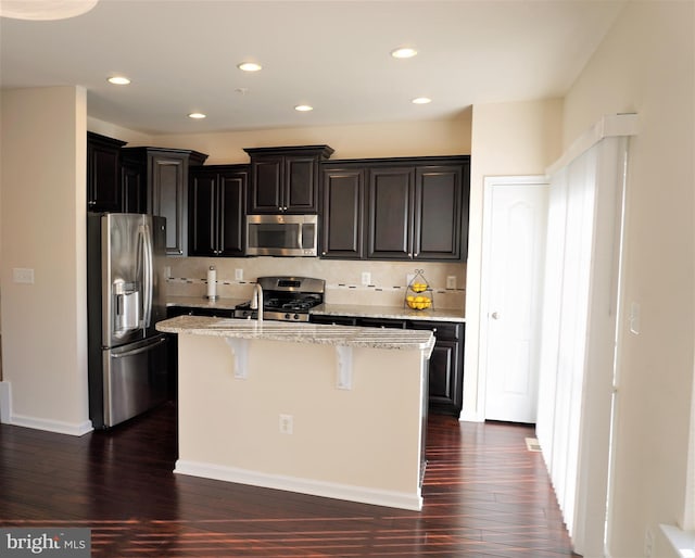 kitchen featuring appliances with stainless steel finishes, dark wood-type flooring, backsplash, a center island with sink, and a breakfast bar area