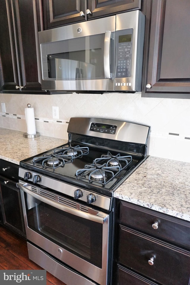 kitchen featuring light stone counters, backsplash, appliances with stainless steel finishes, and dark brown cabinets