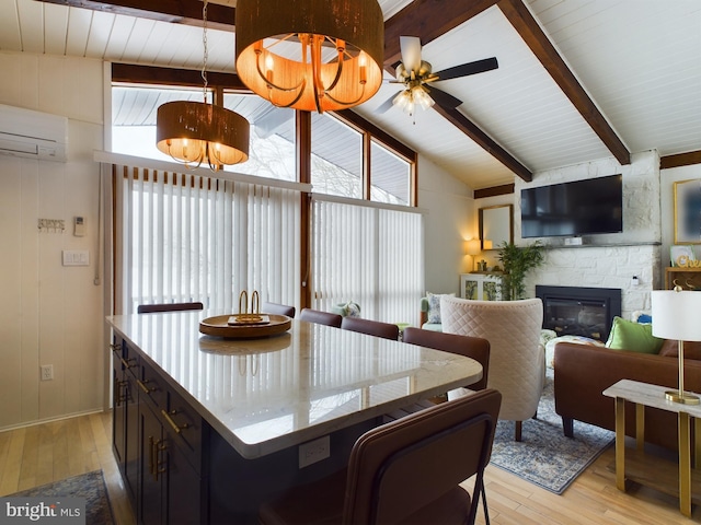 dining space with a wall mounted AC, light wood-type flooring, ceiling fan with notable chandelier, and a stone fireplace