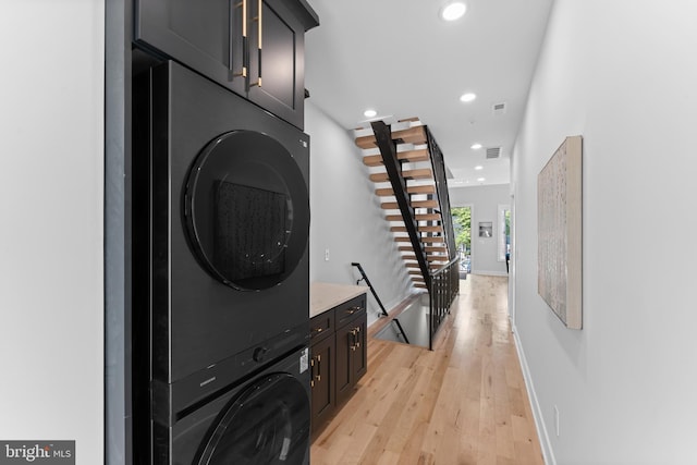 washroom featuring light wood-type flooring, cabinets, and stacked washer and clothes dryer