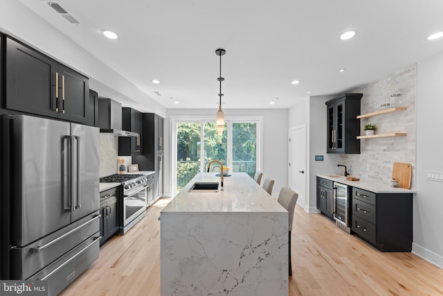 kitchen with beverage cooler, light wood-type flooring, light stone countertops, high quality appliances, and sink