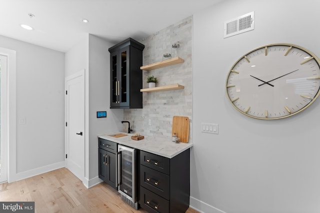 bar featuring beverage cooler, light wood-type flooring, light stone countertops, sink, and backsplash