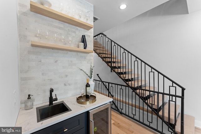 bar with sink, light hardwood / wood-style floors, beverage cooler, and decorative backsplash