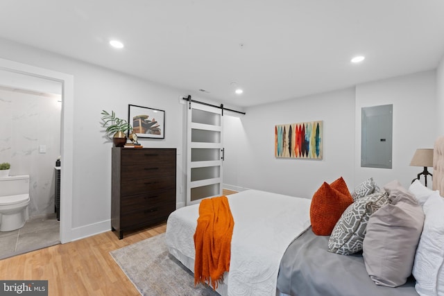 bedroom with light wood-type flooring, connected bathroom, electric panel, and a barn door