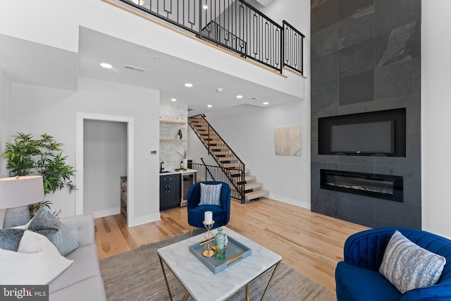 living room with a tiled fireplace, hardwood / wood-style floors, and a towering ceiling