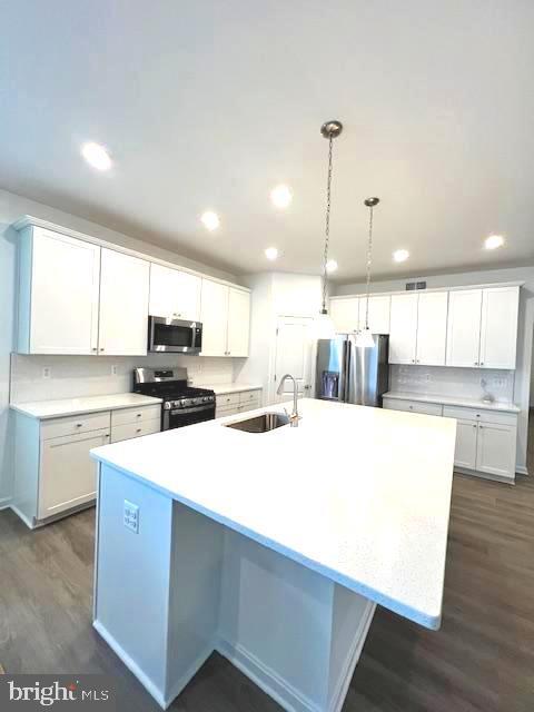 kitchen with sink, white cabinets, appliances with stainless steel finishes, and a center island with sink