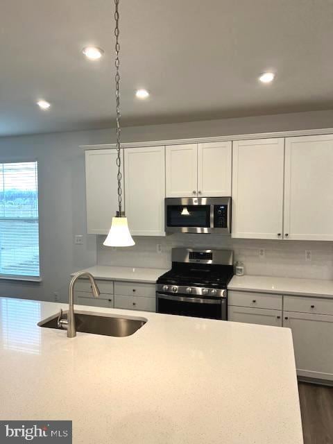 kitchen with pendant lighting, appliances with stainless steel finishes, white cabinets, tasteful backsplash, and sink