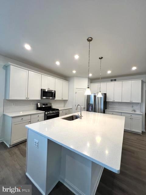 kitchen with appliances with stainless steel finishes, dark wood-type flooring, white cabinetry, sink, and a kitchen island with sink