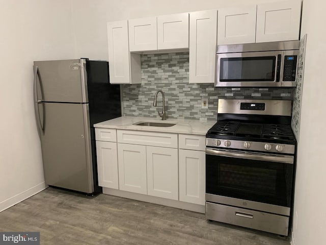 kitchen featuring light stone countertops, backsplash, white cabinets, appliances with stainless steel finishes, and sink