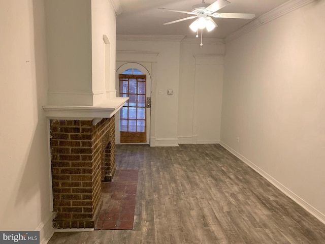 foyer entrance with baseboards, a ceiling fan, ornamental molding, dark wood-style flooring, and a brick fireplace