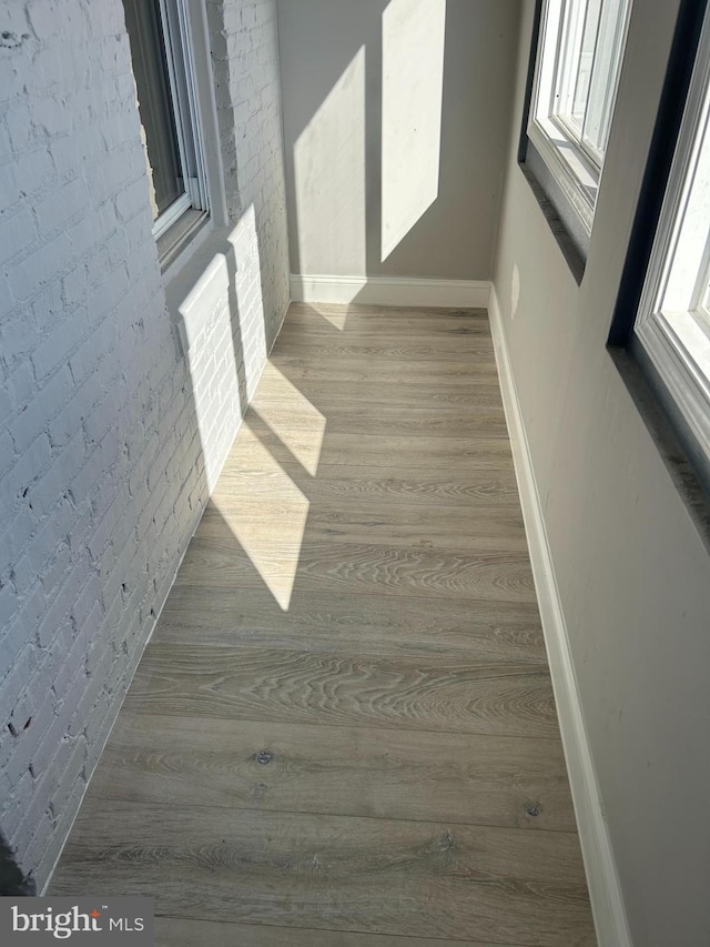 corridor featuring brick wall and light hardwood / wood-style flooring