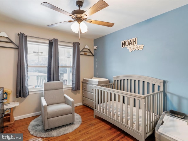 bedroom featuring a crib, ceiling fan, and hardwood / wood-style flooring