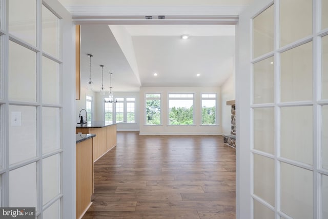 unfurnished living room featuring sink, a stone fireplace, an inviting chandelier, and dark hardwood / wood-style floors