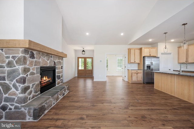 kitchen featuring light brown cabinets, stainless steel fridge with ice dispenser, dark hardwood / wood-style floors, pendant lighting, and a stone fireplace