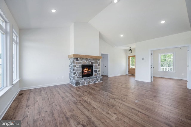 unfurnished living room featuring lofted ceiling, hardwood / wood-style flooring, and a stone fireplace