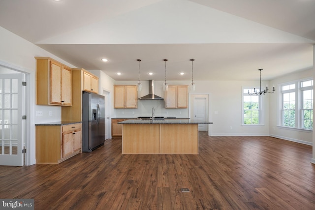 kitchen featuring a kitchen island with sink, stainless steel fridge with ice dispenser, light brown cabinetry, sink, and wall chimney range hood