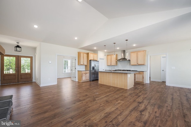 kitchen with vaulted ceiling, french doors, stainless steel fridge with ice dispenser, a center island with sink, and wall chimney range hood