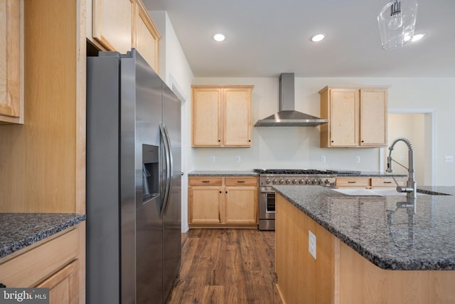 kitchen with dark stone countertops, appliances with stainless steel finishes, dark hardwood / wood-style floors, light brown cabinets, and wall chimney range hood