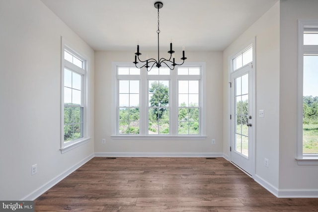 unfurnished dining area featuring dark wood-type flooring, an inviting chandelier, and plenty of natural light