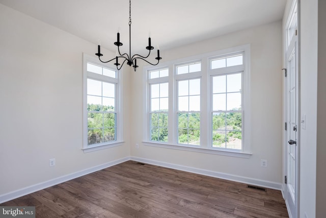 unfurnished dining area with an inviting chandelier, a healthy amount of sunlight, and dark wood-type flooring