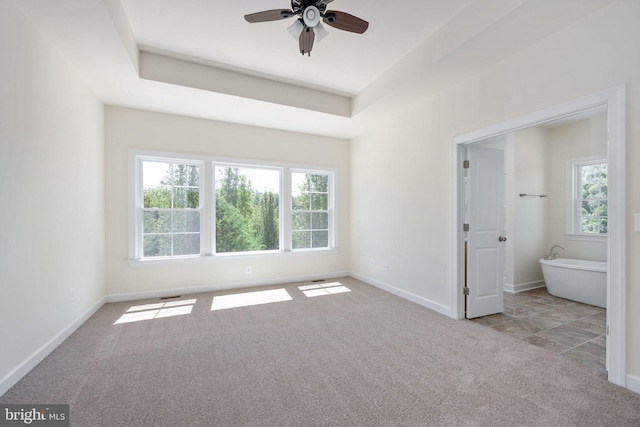 empty room featuring ceiling fan, light carpet, and a tray ceiling