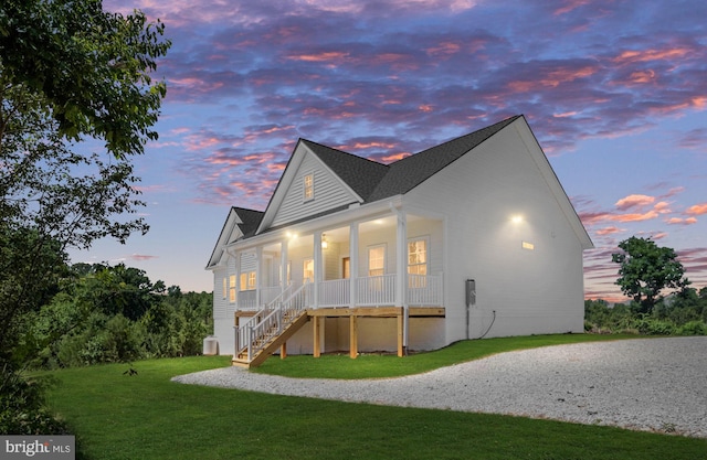 back house at dusk featuring a porch and a yard