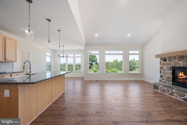 kitchen with dark stone countertops, hanging light fixtures, dark wood-type flooring, light brown cabinets, and sink