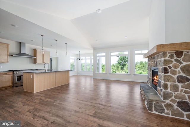 kitchen with a kitchen island with sink, stainless steel stove, light brown cabinetry, a fireplace, and wall chimney range hood