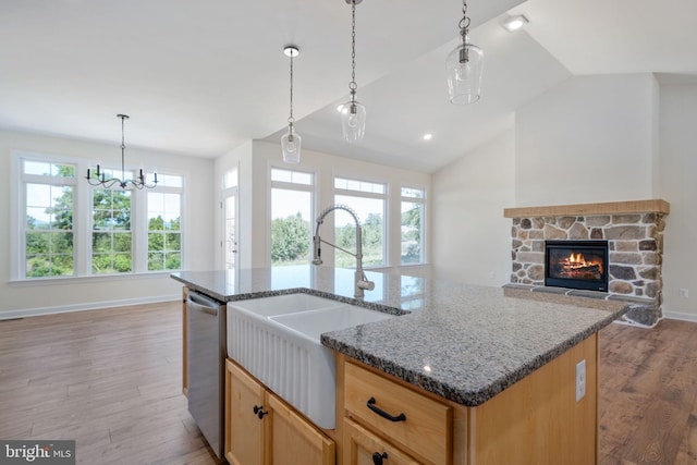 kitchen with sink, stone counters, wood-type flooring, a center island with sink, and a stone fireplace