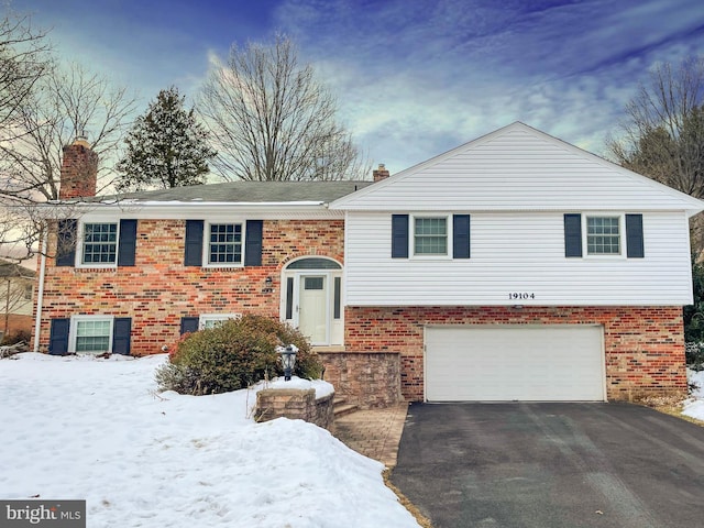 raised ranch with brick siding, driveway, an attached garage, and a chimney