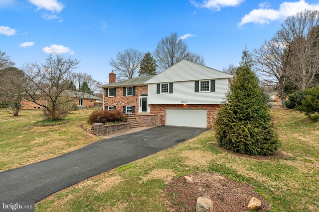 bi-level home featuring brick siding, a front yard, a chimney, a garage, and driveway