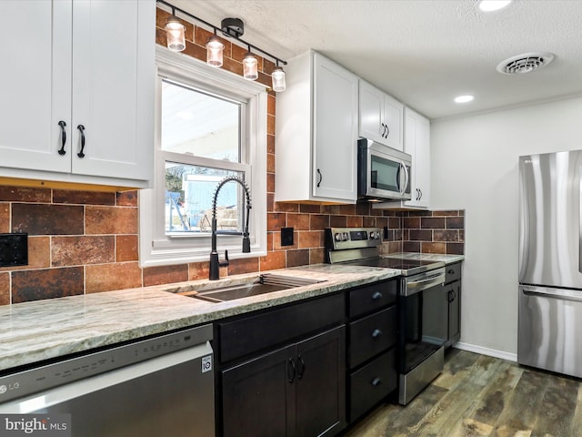 kitchen with appliances with stainless steel finishes, dark wood-type flooring, sink, white cabinetry, and backsplash