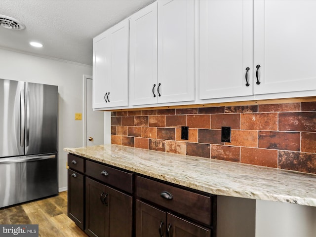 kitchen with white cabinets, dark brown cabinets, light stone counters, and stainless steel refrigerator