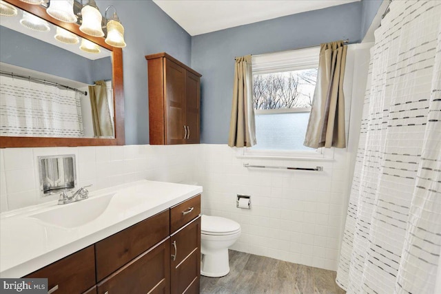 bathroom featuring toilet, walk in shower, tile walls, wood-type flooring, and vanity