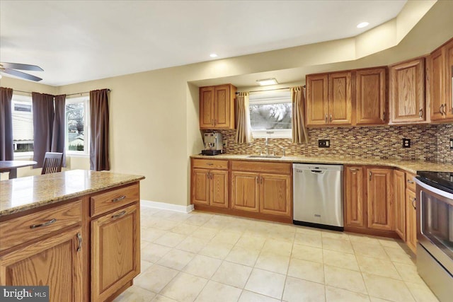 kitchen featuring stainless steel appliances, sink, light stone counters, ceiling fan, and tasteful backsplash