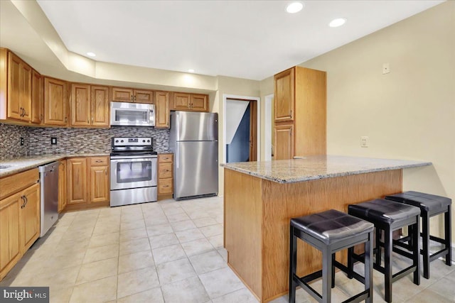 kitchen with a kitchen breakfast bar, stainless steel appliances, light stone countertops, light tile patterned floors, and kitchen peninsula