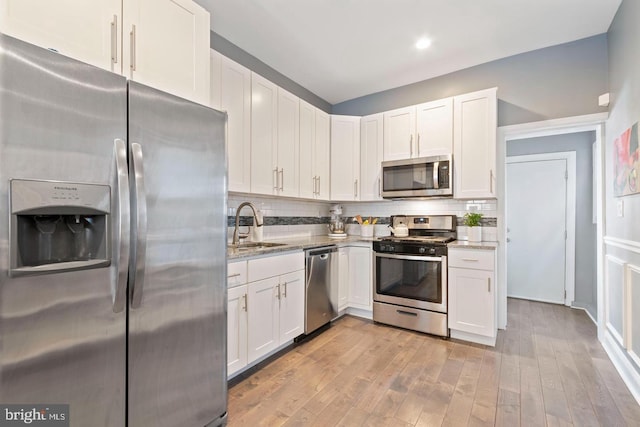 kitchen with appliances with stainless steel finishes, white cabinets, light stone counters, and sink