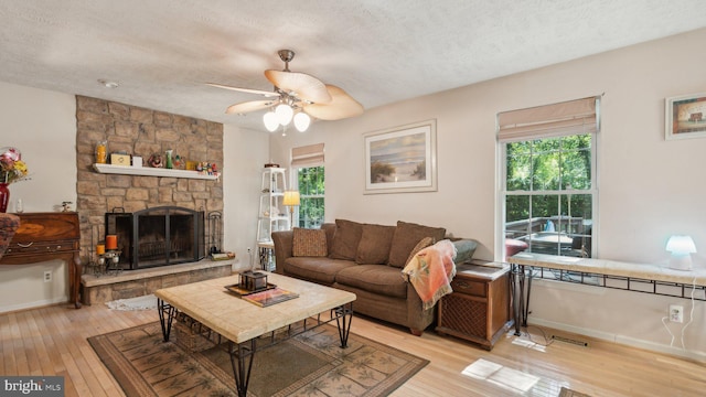 living room featuring ceiling fan, a fireplace, a textured ceiling, and light hardwood / wood-style flooring