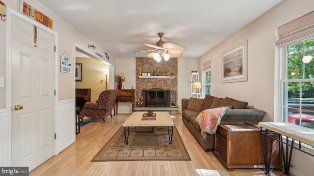 living room with a stone fireplace, ceiling fan, and light hardwood / wood-style flooring