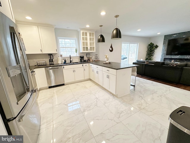 kitchen with kitchen peninsula, pendant lighting, stainless steel appliances, white cabinetry, and sink