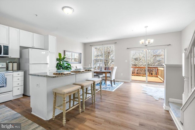 kitchen with pendant lighting, white appliances, light hardwood / wood-style flooring, white cabinets, and dark stone counters