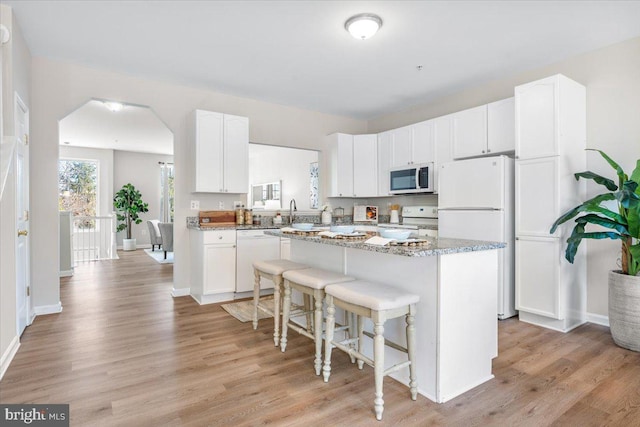 kitchen with light stone counters, white appliances, a breakfast bar area, and white cabinets