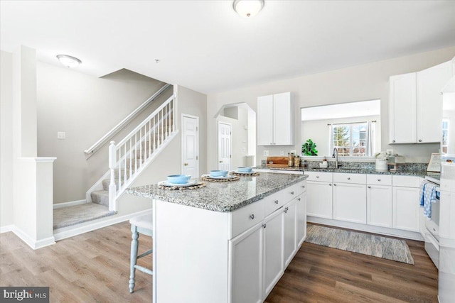 kitchen featuring white cabinetry, hardwood / wood-style floors, light stone countertops, and a center island